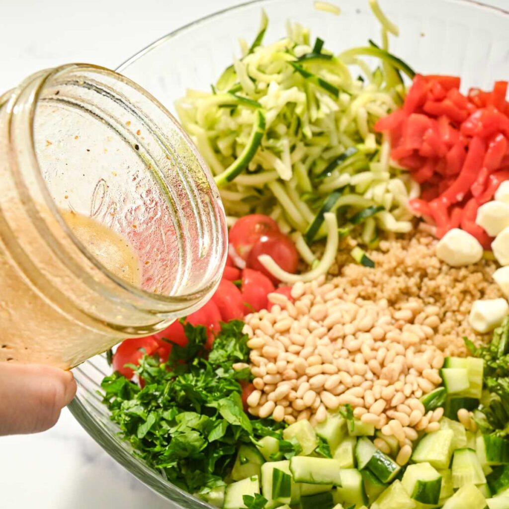 pouring vinaigrette into a bowl of veggies.