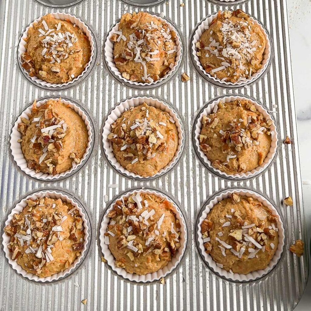 carrot cake protein muffins in a muffin tin topped with coconut and pecans.