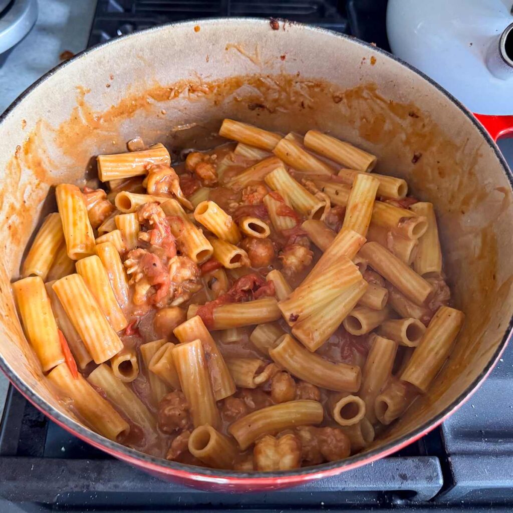 lobster bisque pasta sauce with rigatoni pasta in a pot on the stove.