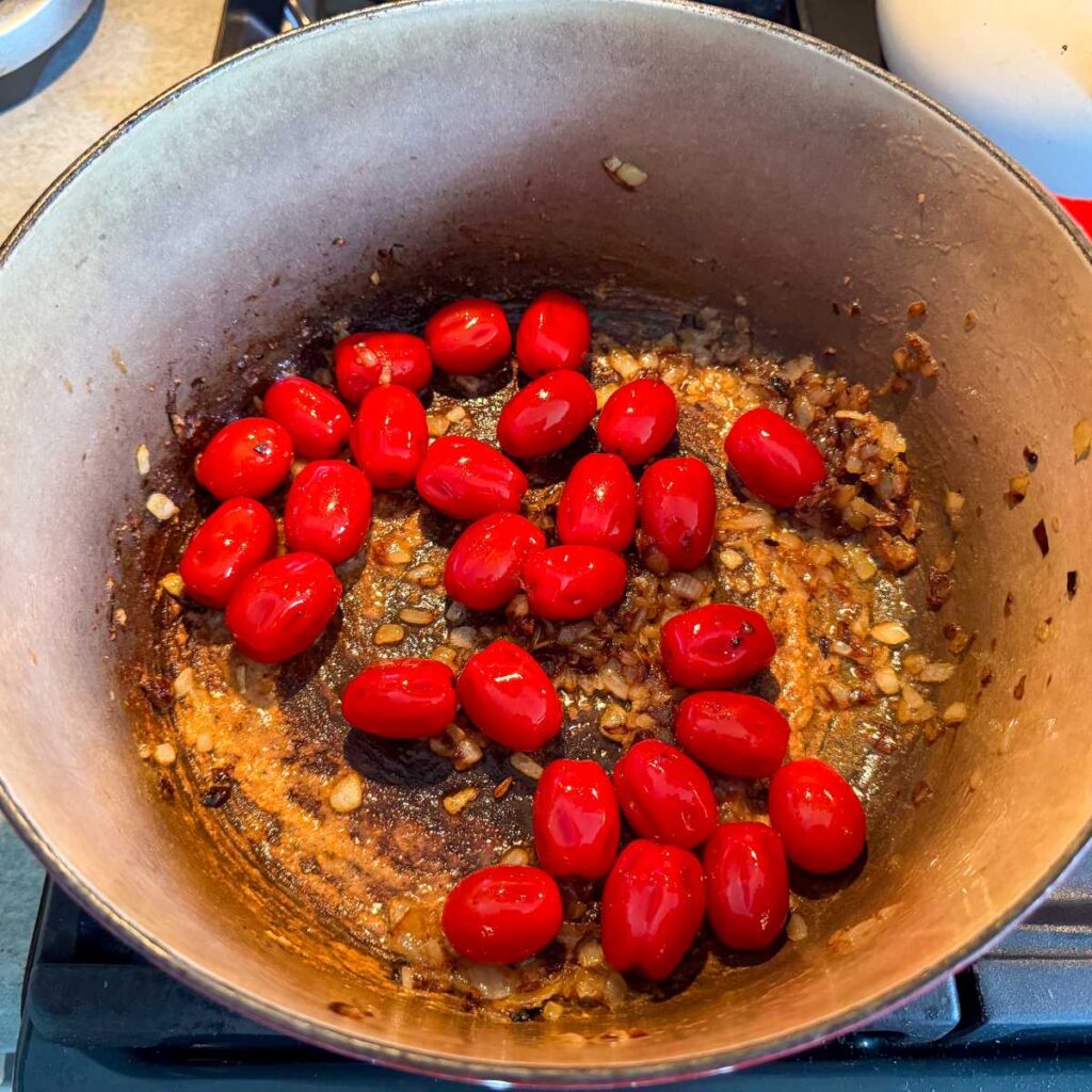 cherry tomatoes cooking in onions in a pot on the stove.